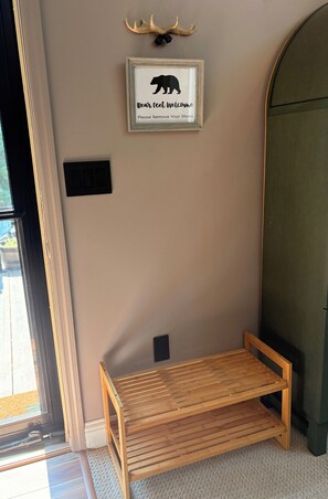 A room with a framed bear silhouette and antlers on the wall, a wooden bench, and a door with a glass panel.