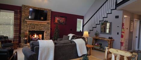 A living room with a fireplace, a sofa, a TV mounted on a stone wall, and a staircase.