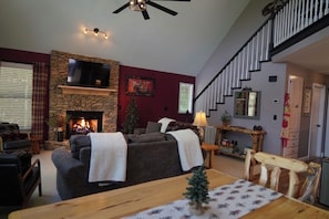 A living room with a fireplace, a sofa, a TV mounted on a stone wall, and a staircase.