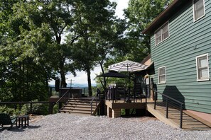 Eine Holzterrasse mit einer Treppe zu einem überdachten Bereich, der von einem Streifen-Sonnenschirm beschattet wird.
