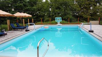 Une piscine équipée d’un panier de basketball, de chaises longues et de parasols.