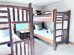 A bunk bed room with a rustic wooden ladder design, a small table with a lamp, and a window providing a view.