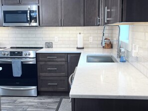 A modern kitchen with stainless steel appliances, dark cabinetry, and a marble countertop.
