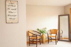 Een kamer met twee rieten stoelen, een gevlochten vaas met planten en een spiegel aan de muur.