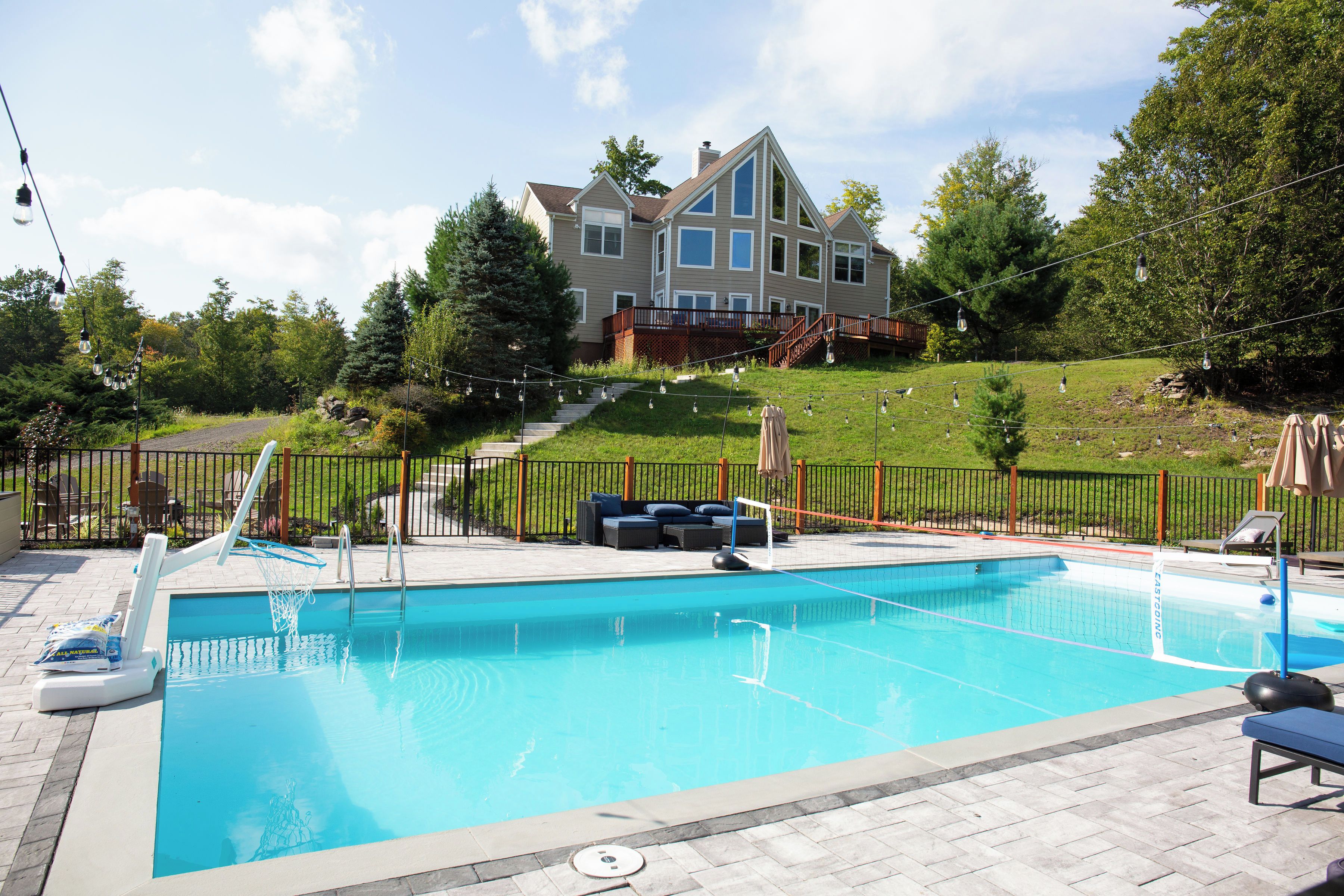 Une piscine avec un panier de basket, des chaises longues et une maison en arrière-plan.
