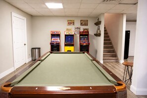 Een pooltafel met drie speelautomaten, een prullenbak en een trap.