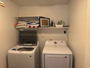 A laundry room with a front-loading washer and dryer, a shelf with folded towels, and a framed picture. - Comfortable & Relaxing Gilbert Oasis with Heated Pool (Gilbert)