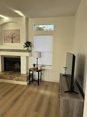 A living room with a fireplace, a television, and a window with blinds. - Comfortable & Relaxing Gilbert Oasis with Heated Pool (Gilbert)