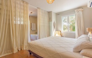 Un dormitorio con cama, ventana y baño visible tras una cortina.