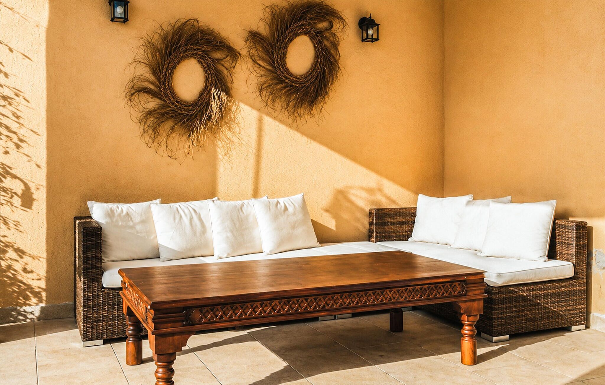 A wicker sofa with white cushions, a wooden coffee table, and two wall-mounted lanterns.