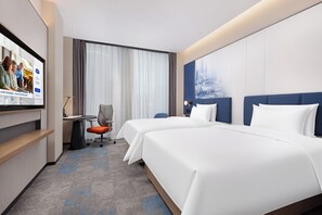Une chambre d’hôtel avec deux lits, un bureau, une chaise et un écran de télévision diffusant une publicité pour l’hôtel.