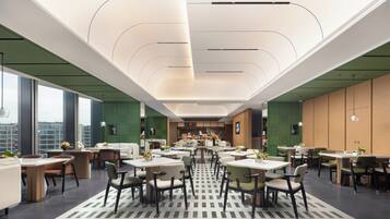 A modern dining area with high ceilings, large windows, and a variety of seating arrangements.