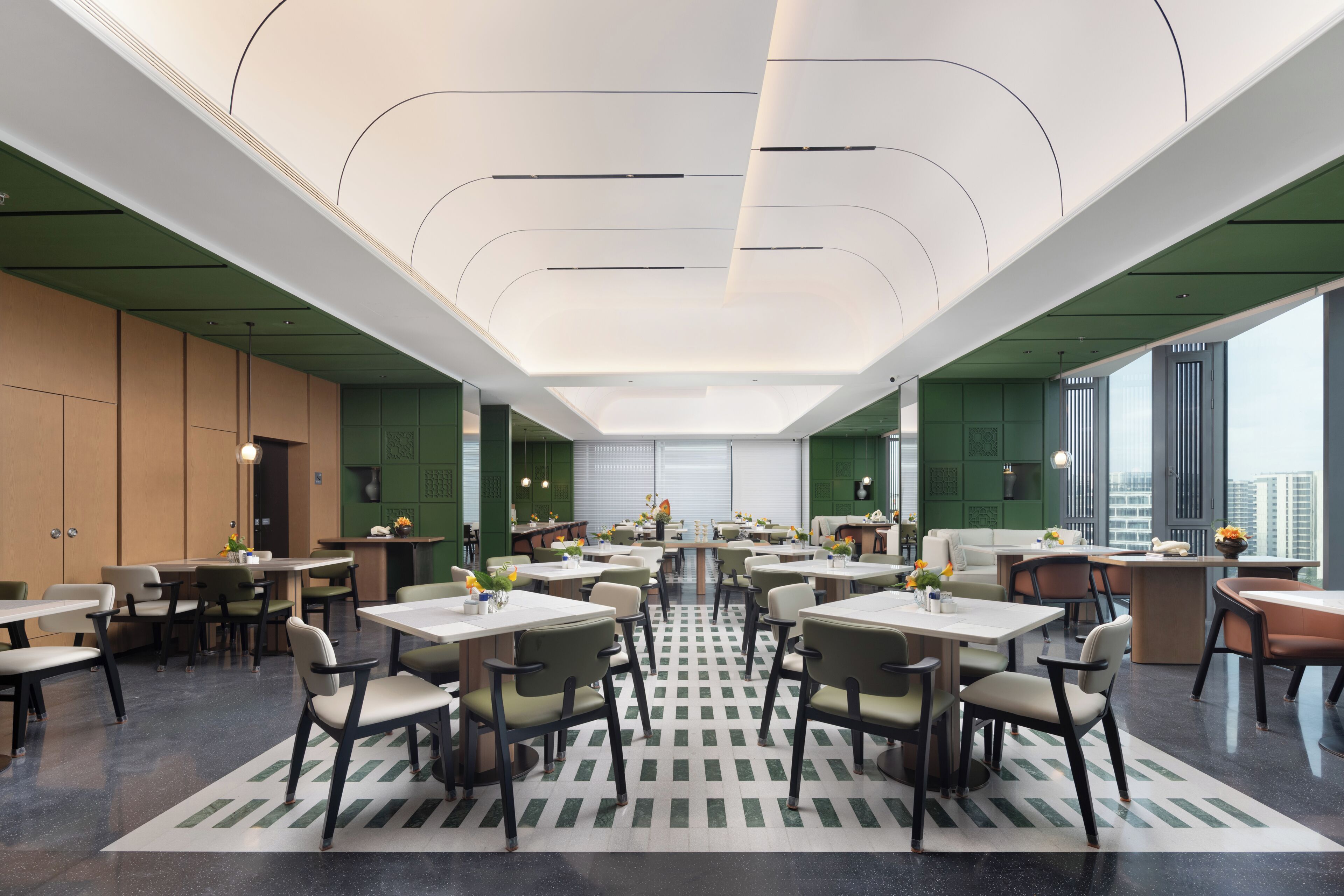 A spacious dining area with multiple tables and chairs, a patterned floor, and large windows offering a view of the city.