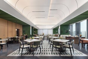 Un amplio comedor con varias mesas y sillas, un suelo con diseño y grandes ventanales que ofrecen vistas a la ciudad.