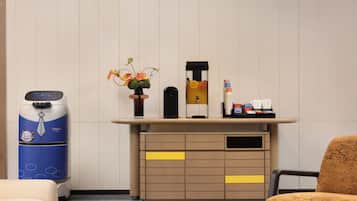 A hotel room with a minibar, a water dispenser, a flower vase, and a small table with toiletries.