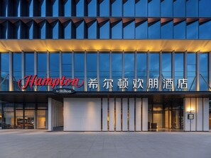 L’entrée d’un hôtel, avec une façade moderne, de grandes fenêtres et une enseigne bien visible.