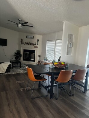A dining area with a black table, four orange chairs, a ceiling fan, and a fireplace with a welcome sign above it. - Lake Livingston 4BR Retreat with Huge Private Dock for Fishing & Boating (Onalaska)