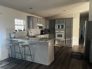 A modern kitchen with a central island, bar stools, a microwave, oven, and a coffee maker. - Lake Livingston 4BR Retreat with Huge Private Dock for Fishing & Boating (Onalaska)