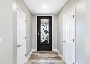A hallway with a wooden floor, white doors, and a frosted glass door with a bird design. - Bay-view 5BR Gulf Shores home with 5.5 baths, sleeps 12, and easy beach access. (Gulf Shores)