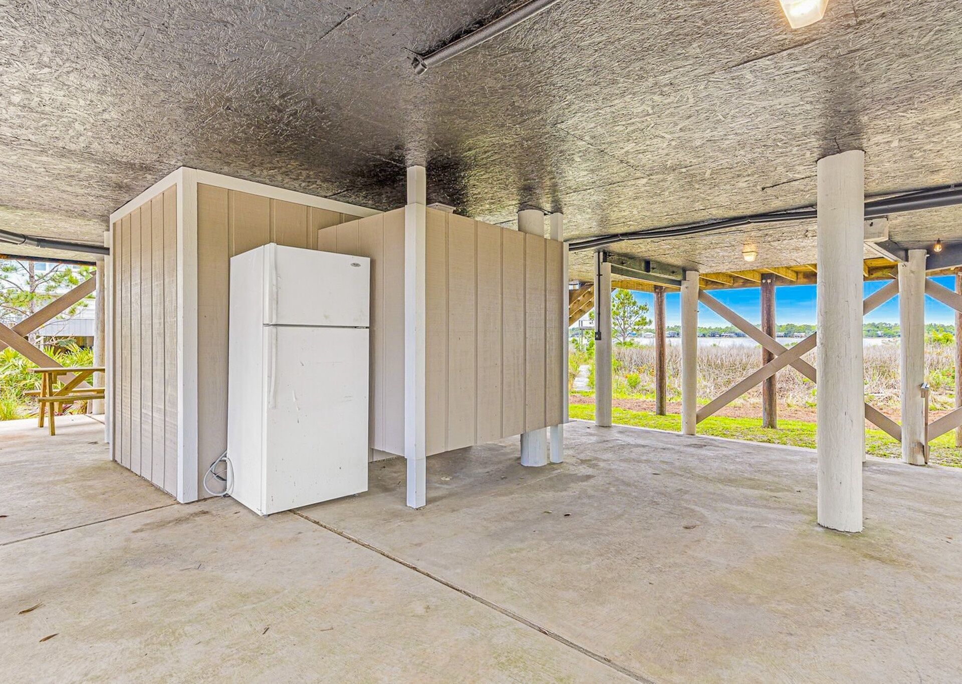 Un espacio exterior cubierto con un refrigerador blanco, bancos de madera y vistas al exterior.
