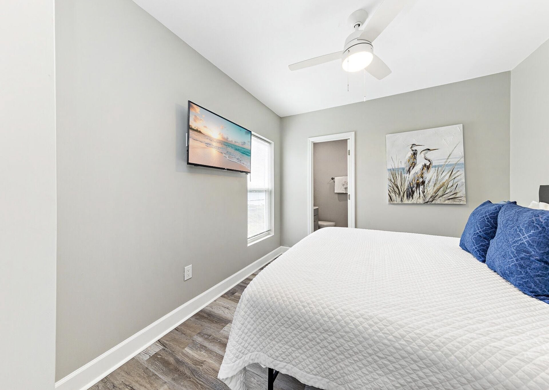 A bedroom with a bed, a ceiling fan, a TV, and artwork on the walls.