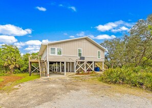 A two-story house with a porch and a covered area, surrounded by greenery. - Bay-view 5BR Gulf Shores home with 5.5 baths, sleeps 12, and easy beach access. (Gulf Shores)