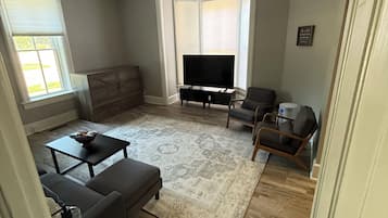 Una sala de estar con ventilador de techo, televisión de pantalla plana, sofá, mesa de centro y alfombra estampada.