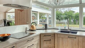 A modern kitchen with a large window, wooden cabinetry, and a kettle on the counter. - Amazing home in Bjert with sauna (Bjert)