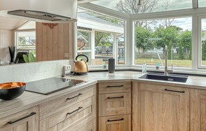 Eine moderne Küche mit großem Fenster, Holzschränken und einem Wasserkocher auf der Arbeitsfläche.