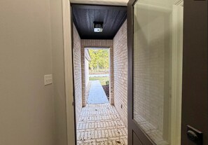 En smal gang med murstensvægge og betongulv, der fører til et udendørs område.