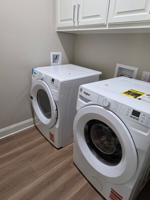 A laundry room with two front-loading washing machines and a dryer, white cabinetry above, and a wooden floor.
