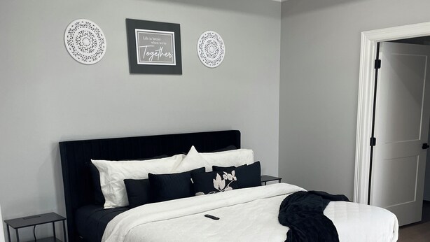 Un dormitorio con cama negra, ropa de cama blanca y alfombras estampadas.