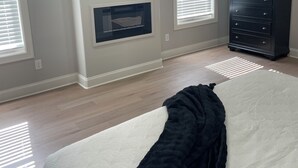Un dormitorio con cama, televisor montado en la pared, cómoda y chimenea.