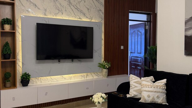 Ein modernes Wohnzimmer mit Flachbildfernseher an einer Marmorwand, einer schwarzen Couch, einem weißen Couchtisch und einer außergewöhnlichen Deckenleuchte.