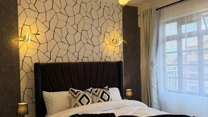 Ein modernes Schlafzimmer mit Wand im geometrischen Muster, einer gepolsterten Kopfstütze und einem großen Fenster mit Vorhängen.