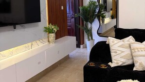 Ein modernes Wohnzimmer mit Flachbildfernseher, einer schwarzen Couch, einem Spiegel und einer Topfpflanze.