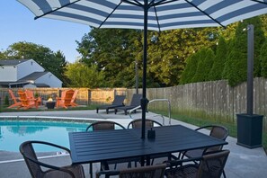 Ein Garten mit Schwimmbad, Liegestühlen, einem Tisch mit Stühlen und einem Sonnenschirm.