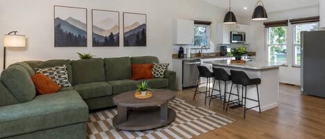 En moderne stue med en hjørnesofa, et sofabord og et køkkenområde med en bar og siddepladser.