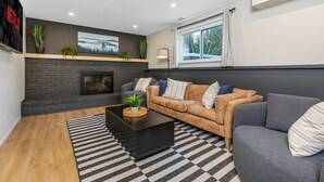 A modern living room with a fireplace, a sofa set, a coffee table, and a large window with curtains. - Pool, Hot tub and Gameroom! (Columbus)