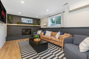 Ein modernes Wohnzimmer mit Kamin, einer Sofagarnitur, einem Couchtisch und einem großen Fenster mit Vorhängen.