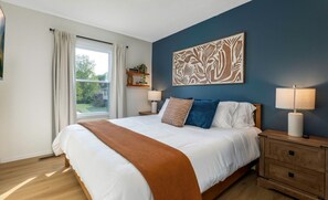 A bedroom with a large bed, two bedside tables with lamps, a window with curtains, and a wall art piece. - Pool, Hot tub and Gameroom! (Columbus)