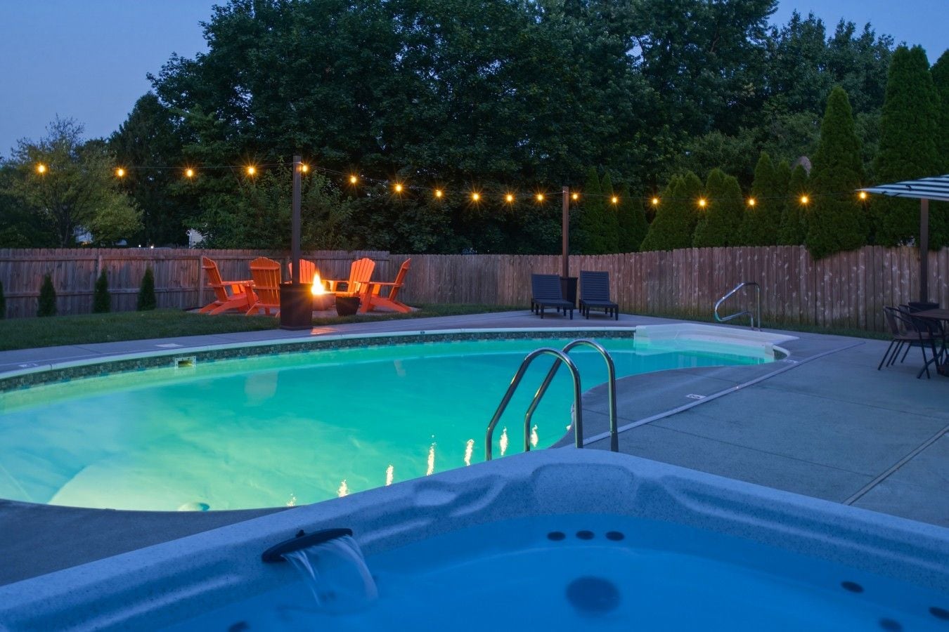 Ein Garten mit Swimmingpool, Whirlpool, Gartenmöbeln und Lichterketten.