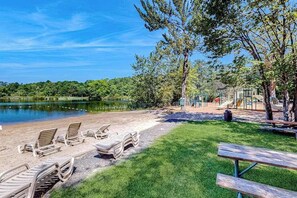 A lakeside park with a sandy beach, lounge chairs, a picnic table, and playground equipment. - Pocono Home with Hot Tub, EV Charge, Pool & Tennis (Tobyhanna)