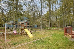 A backyard with a wooden playhouse, a slide, and a swing set. - Pocono Home with Hot Tub, EV Charge, Pool & Tennis (Tobyhanna)