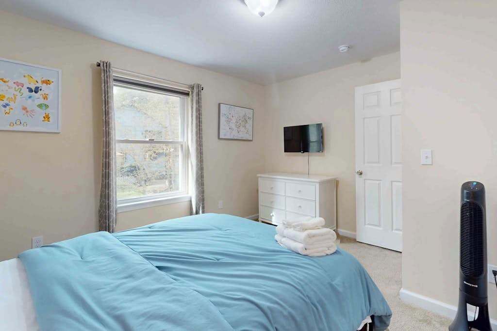 A bedroom with a bed, a dresser, a television, and a window.