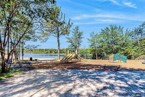 A park with a playground, benches, and a lake in the background. - Pocono Home with Hot Tub, EV Charge, Pool & Tennis (Tobyhanna)