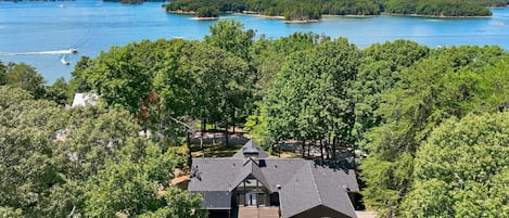 A lakeside property with a swimming pool, surrounded by dense trees and a view of the lake.