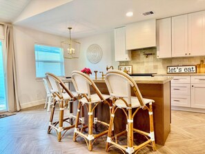 A kitchen with white cabinetry, a central island with bar stools, a chandelier, and a 'let's eat' sign. - Inviting Gateway Near Galveston Beach for families,friends,business travelers. (La Marque)