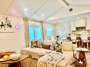 Ein modernes Wohnzimmer mit Sofa, Sesseln, einem Esstisch und einer Küchenzeile.