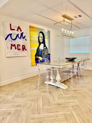 A modern dining area with a glass table and chairs, a ceiling light fixture, and artwork on the walls. - Inviting Gateway Near Galveston Beach for families,friends,business travelers. (La Marque)